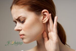 Woman holding her ear with an uncomfortable expression, illustrating symptoms like crackling in the ear