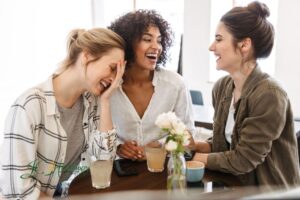 Three friends sitting together at a café table, smiling and talking while enjoying drinks