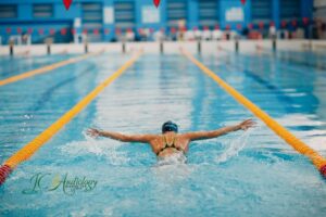 Swimmer performing a butterfly stroke in an indoor pool, illustrating water exposure that can lead to swimmer’s ear.
